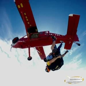 Paracadutista che si stacca dal portellone dell'aereo rosso della scuola
